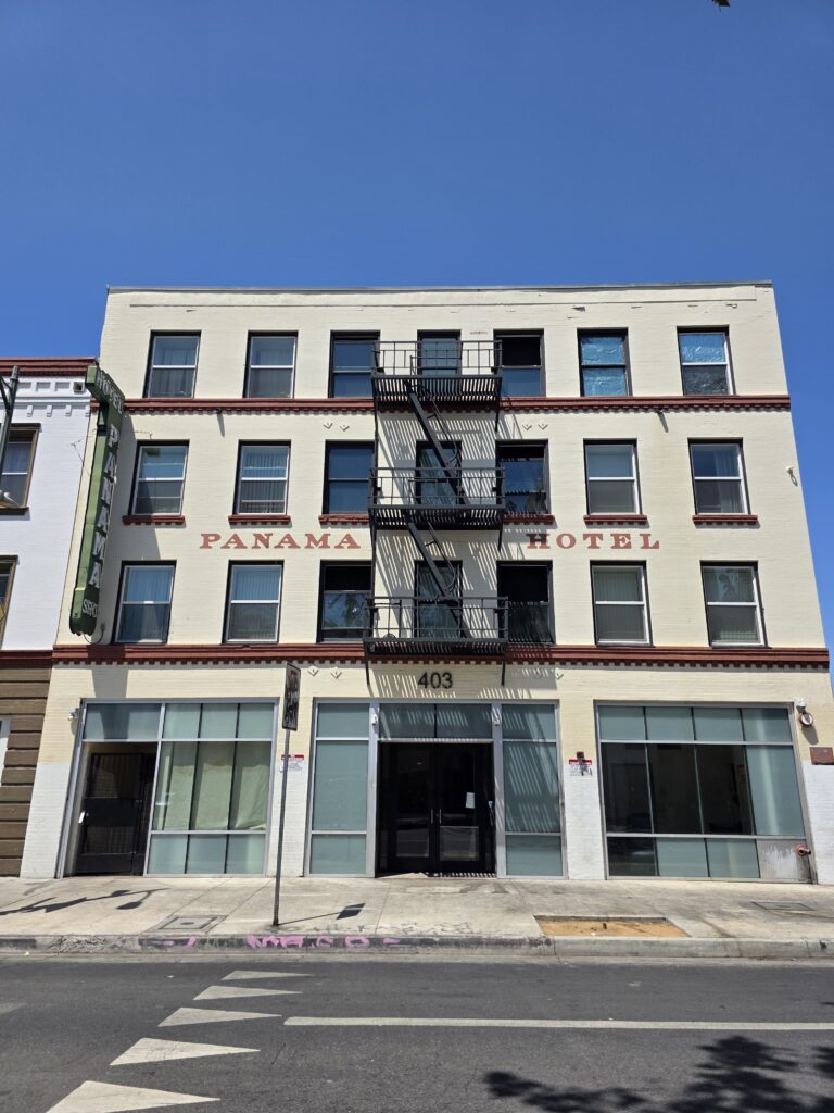 The historic Panama Hotel at 403 E. 5th Street in Downtown Los Angeles — a wonderfully intact early 20th-century brick hotel building with a simple, utilitarian façade, original fire escape, rows of tall sash windows, and beautifully faded hand-painted “PANAMA HOTEL” lettering across the front.