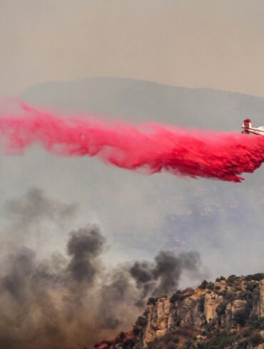 Airplane drops fire retardant from low elevation above the treetops of an active California fire