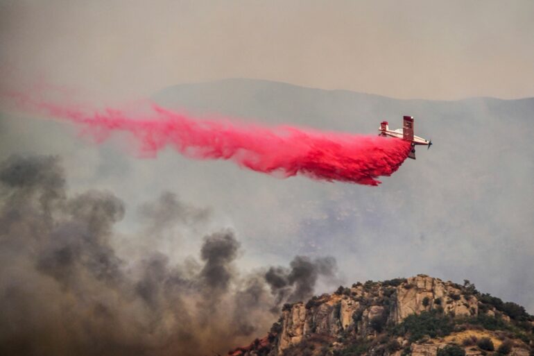 Airplane drops fire retardant from low elevation above the treetops of an active California fire