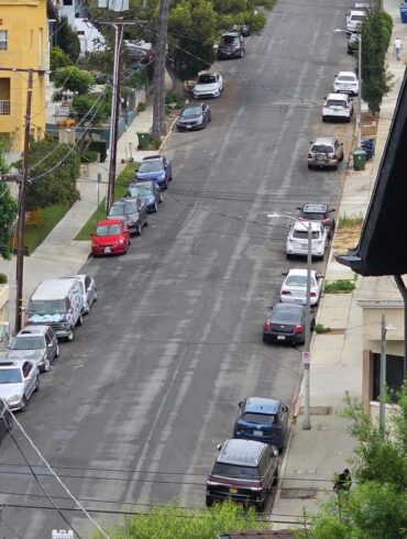 Steep residential street in Echo Park, Los Angeles, lined with parked cars and apartment buildings, seen from above