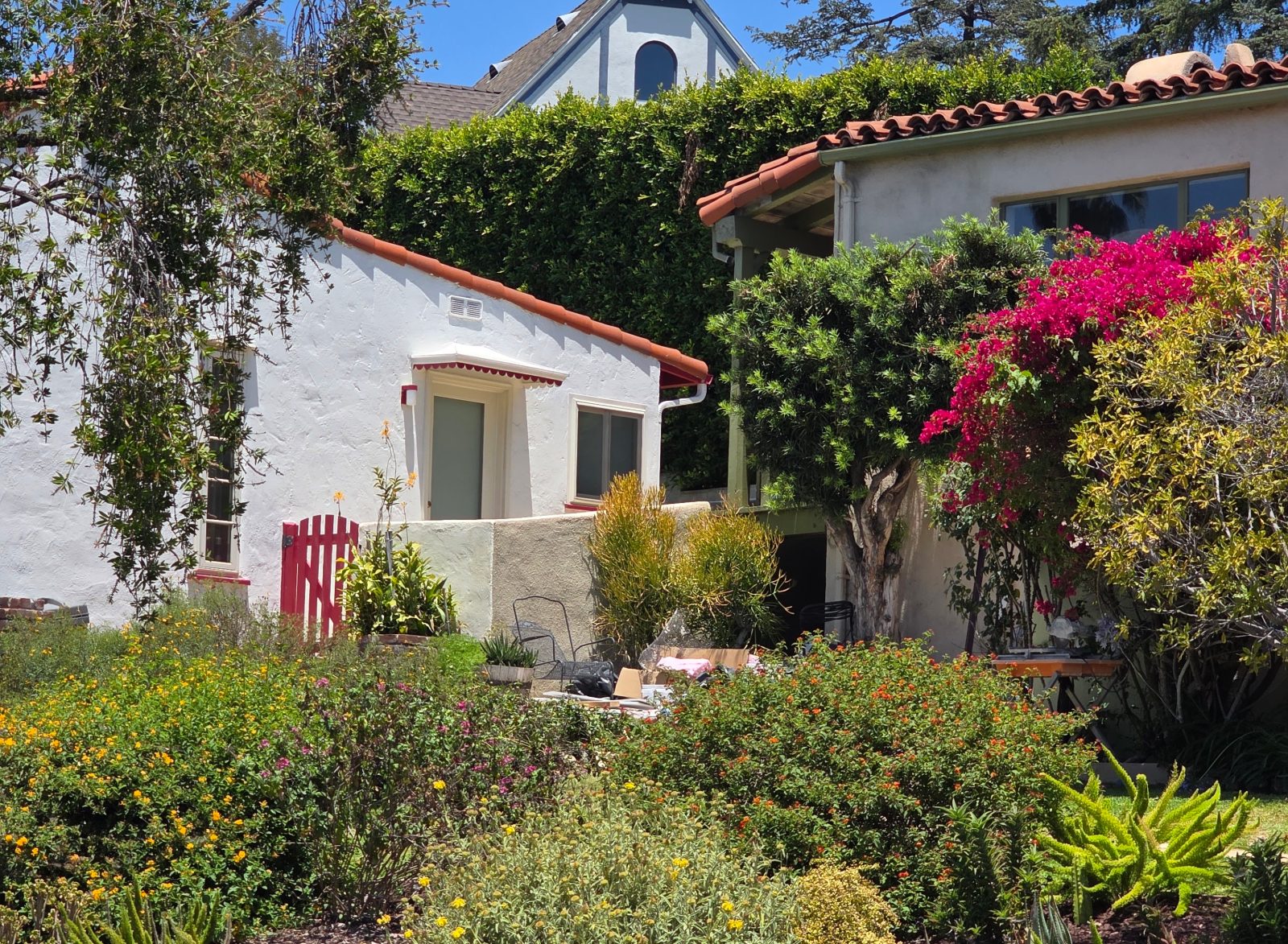 White stucco Spanish style homes with red tile roofs, a red garden gate and pink bougainvillea in Eagle Rock, Los Angeles